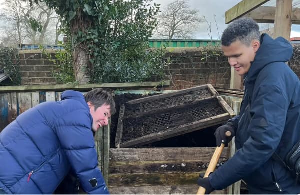 Two people happily turning a compost pile